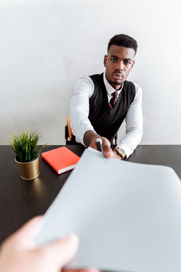 African American businessman handing a document across the desk in an office setting.